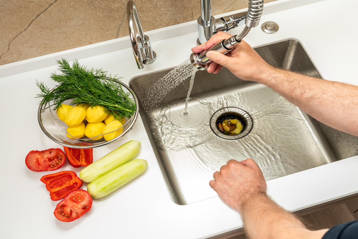 A man washes food waste into a dispenser - learn how to protect your garbage disposal with tips from Zest.