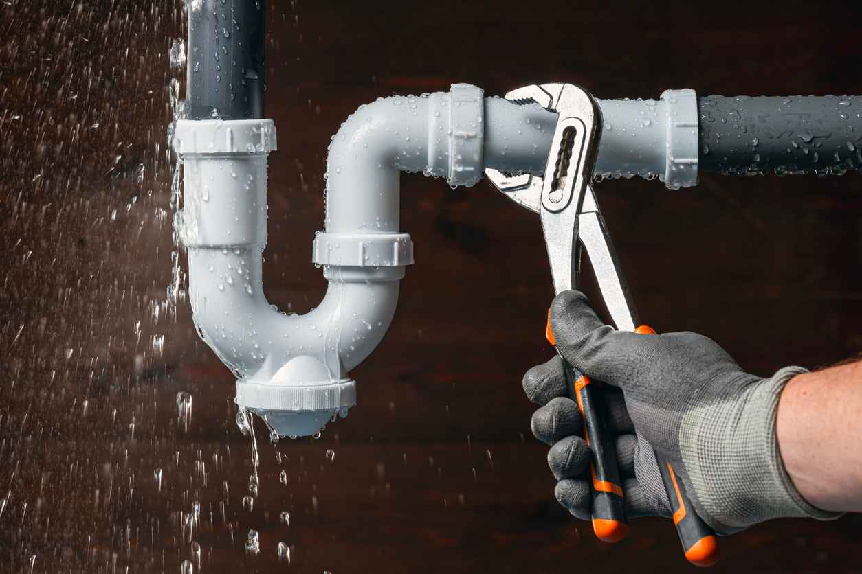 Close up of a plumber hand fixing a water leak in a sink drain siphon pipe with an adjustable pliers.
