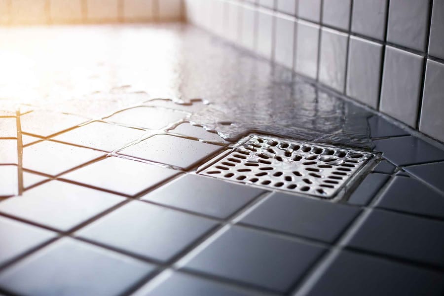 Water flowing to square shower drain on tiled floor of modern enclosure in bathroom.